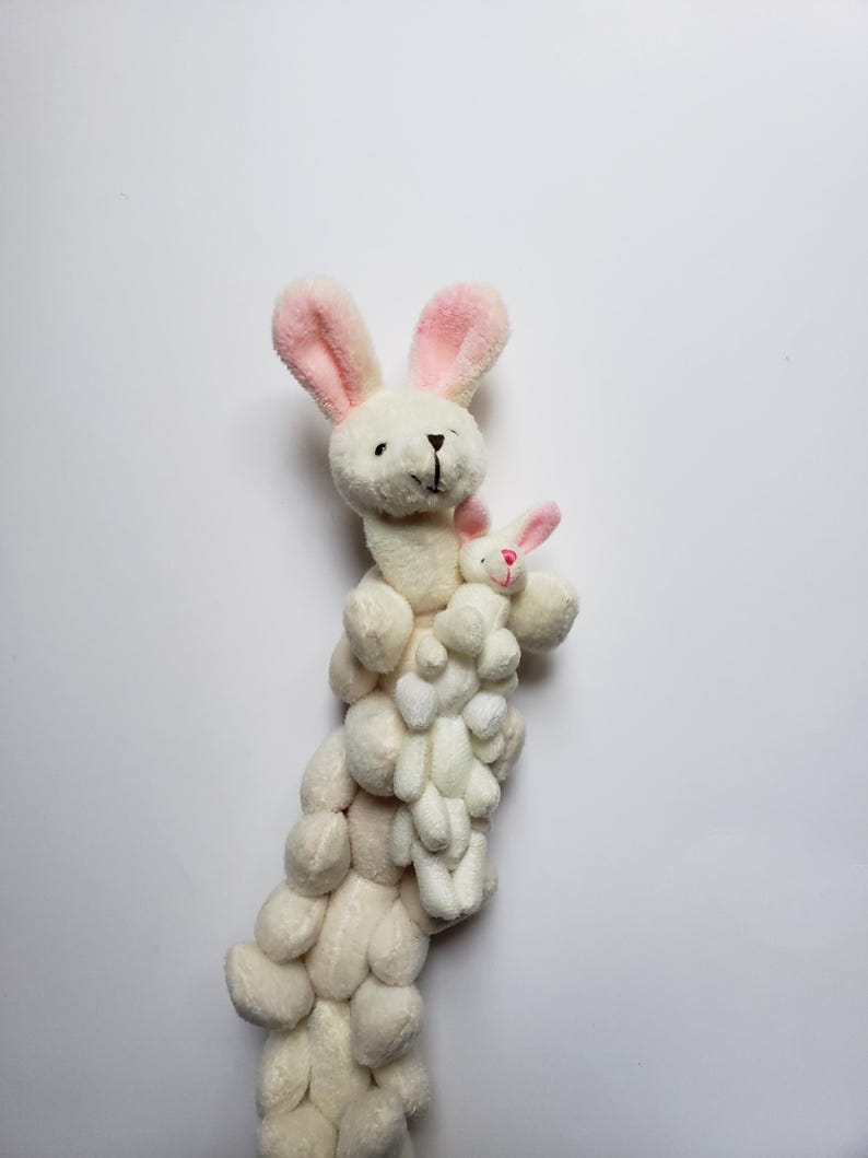 May include: A white plush bunny with pink ears holding a smaller white plush bunny with pink ears. The bunnies are stacked on top of each other, creating a tower of plush bunnies.