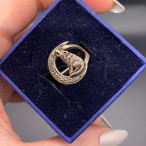 May include: A silver ring with a wolf howling at the moon design. The ring is in a blue velvet box.