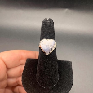 May include: A silver ring with a heart-shaped white stone set in the center.