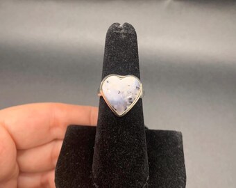 May include: A silver ring with a heart-shaped white stone set in the center.