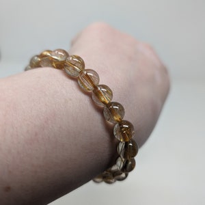 May include: A gold and brown beaded bracelet with gold flecks throughout the beads.