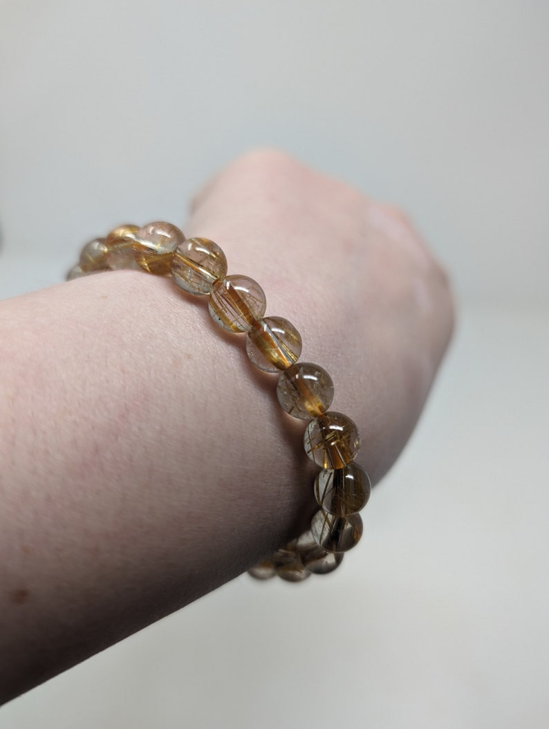 May include: A gold and brown beaded bracelet with gold flecks throughout the beads.