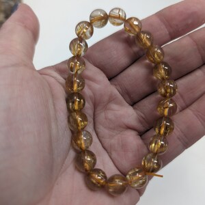May include: A gold and clear quartz bracelet with gold inclusions. The bracelet is made of round beads and is strung on a clear elastic cord.