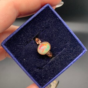 May include: A rose gold ring with a colorful opal gemstone. The ring is in a blue velvet ring box.