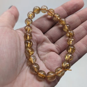 May include: A gold and clear crystal bracelet with gold flecks throughout. The bracelet is made of round beads and is strung on a clear elastic cord.