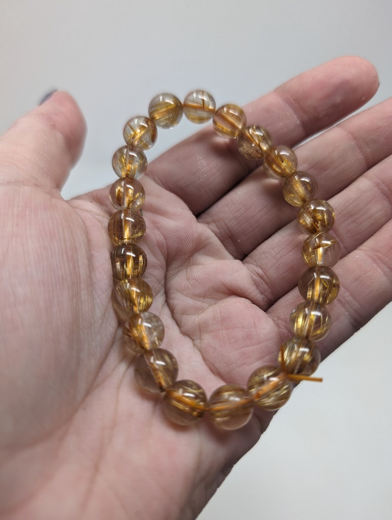 May include: A gold and clear crystal bracelet with gold flecks throughout. The bracelet is made of round beads and is strung on a clear elastic cord.