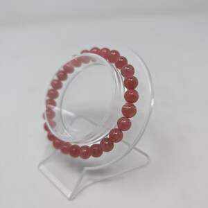 May include: A pink gemstone bracelet with round beads on a clear display stand.
