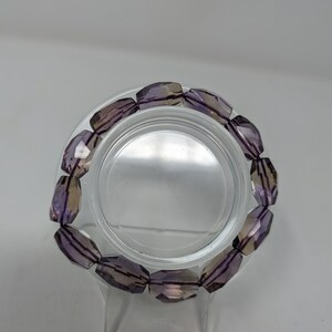 May include: A purple and clear crystal bracelet with faceted beads. The bracelet is on a clear display stand.