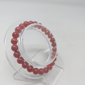 May include: A pink gemstone bracelet with round beads on a clear plastic stand.