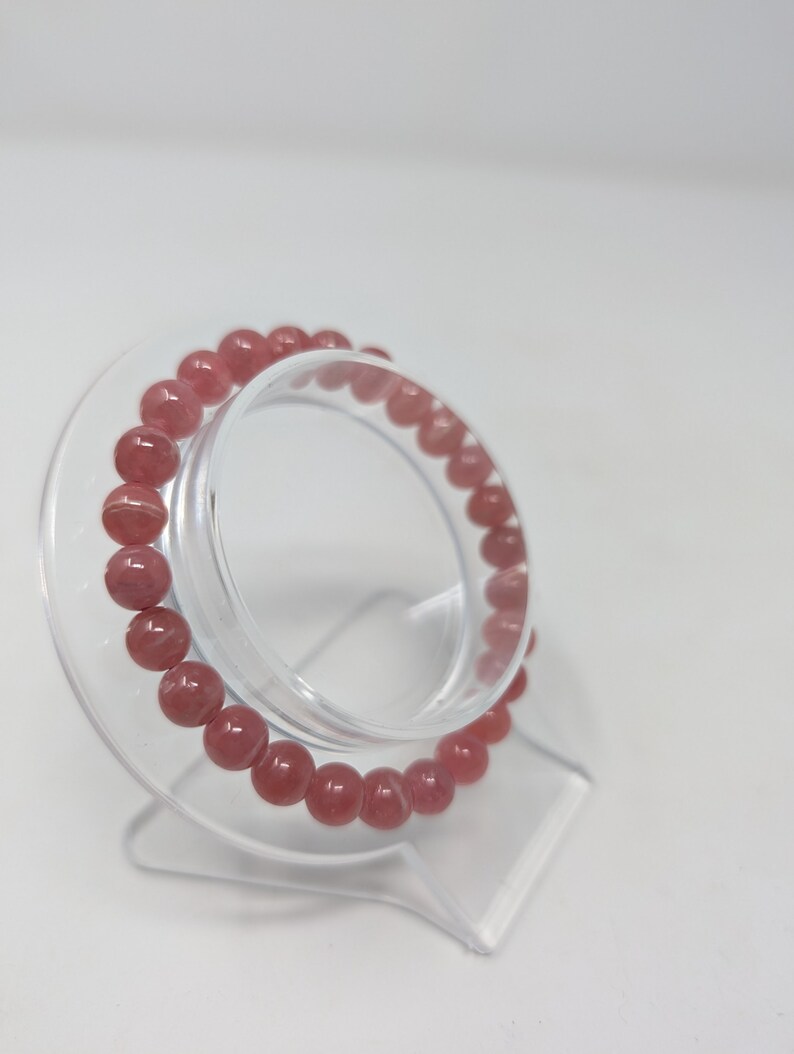 May include: A pink gemstone bracelet with round beads on a clear plastic stand.