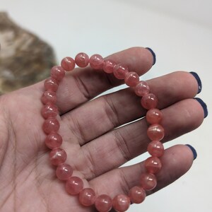 May include: A pink gemstone bracelet with round beads. The bracelet is made of natural stones and is approximately 7 inches in length.