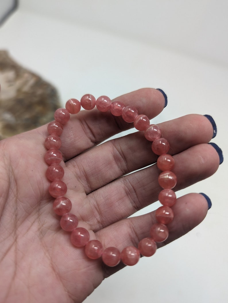May include: A pink gemstone bracelet with round beads. The bracelet is made of natural stones and is approximately 7 inches in length.
