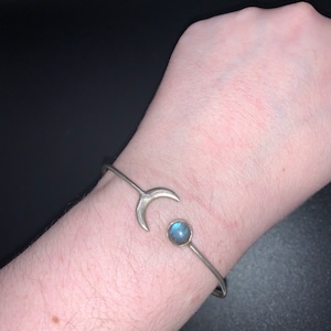 May include: A silver bracelet with a crescent moon charm and a blue labradorite gemstone.