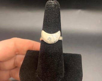 May include: A silver ring with a white crescent moon design. The ring is on a black ring display stand.
