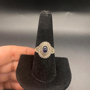 May include: A silver ring with an oval-shaped purple gemstone set in a detailed filigree design.