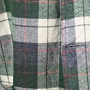 K&ouml;nnte beinhalten: Nahaufnahme einer gr&uuml;n, wei&szlig; und marineblau karierten Jacke. Die Jacke hat einen Knopfverschluss und einen strukturierten Stoff. Rote Linien akzentuieren das Karomuster und schaffen einen klassischen, zeitlosen Look.