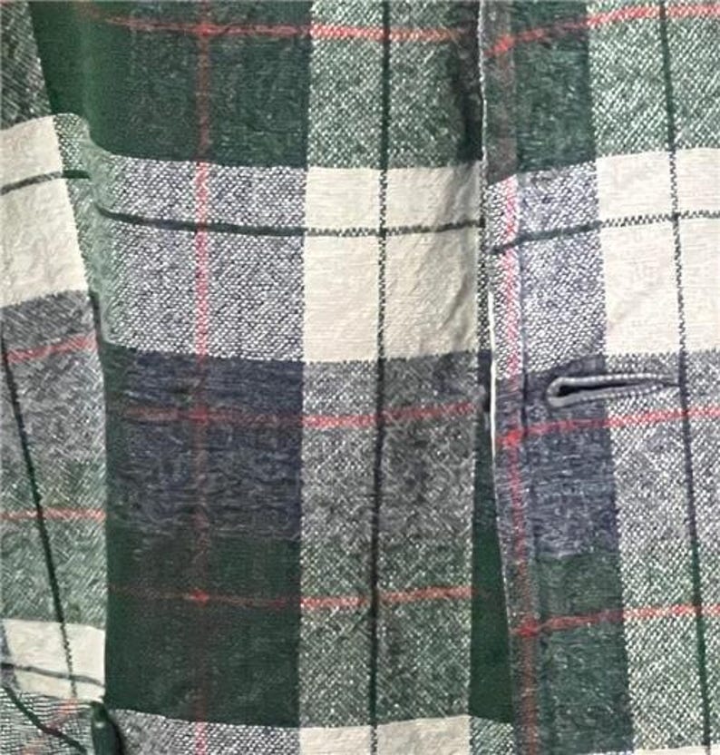 K&ouml;nnte beinhalten: Nahaufnahme einer gr&uuml;n, wei&szlig; und marineblau karierten Jacke. Die Jacke hat einen Knopfverschluss und einen strukturierten Stoff. Rote Linien akzentuieren das Karomuster und schaffen einen klassischen, zeitlosen Look.