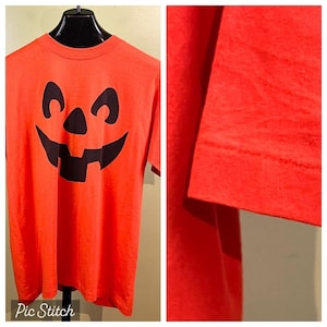 May include: Orange t-shirt with a black jack-o'-lantern face graphic.