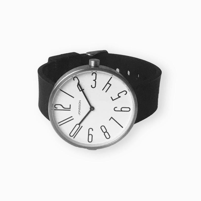 May include: A black leather wristband watch with a white face and black numbers. The watch face has the text "J&Ouml;NSSON" printed on it.