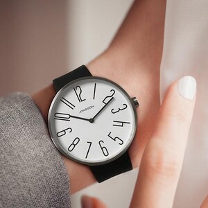 May include: A black and silver wristwatch with a white face and black numbers. The watch has a black leather band.