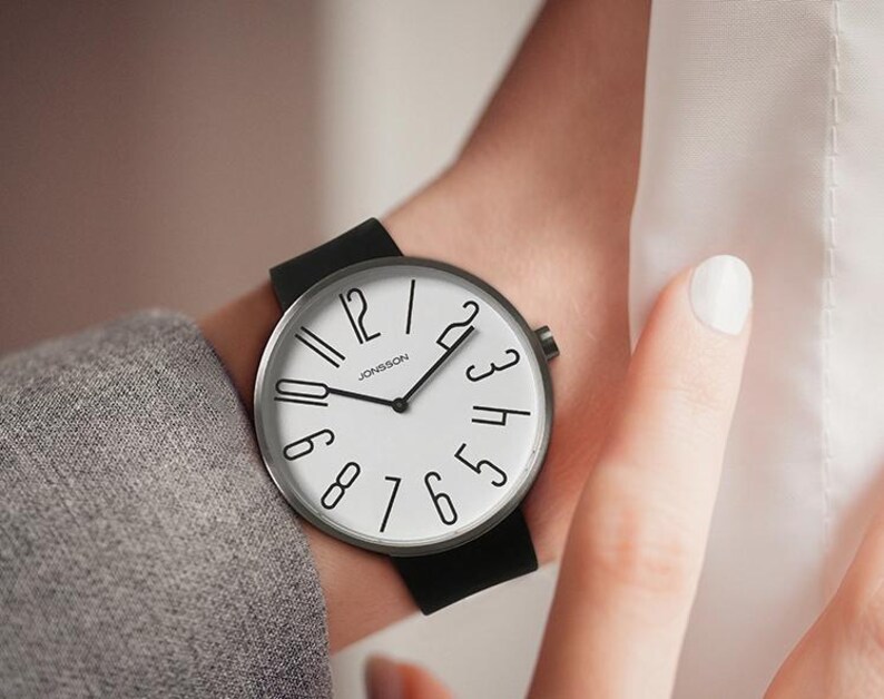 May include: A black and silver wristwatch with a white face and black numbers. The watch has a black leather band.