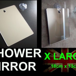 Puede incluir: Un espejo de ducha rectangular plateado, con un agujero para colgarlo y una ventosa. El espejo refleja el entorno. El texto "SHOWER MIRROR" está debajo. Mide 18 cm x 13 cm.