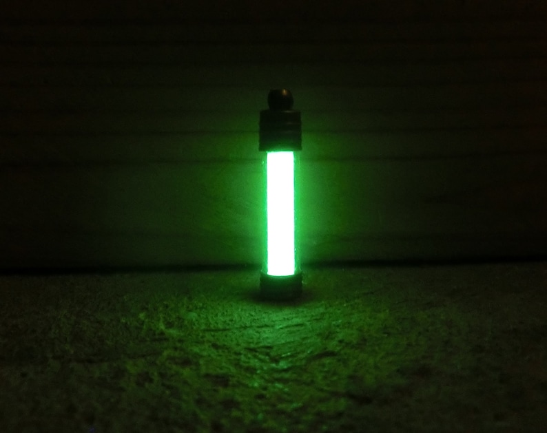 Puede incluir: Un objeto cil&iacute;ndrico verde brillante con una tapa y base oscuras. El objeto emite una luz verde brillante y vibrante, creando un contraste llamativo con el fondo oscuro. El efecto general es una est&eacute;tica futurista o cient&iacute;fica.