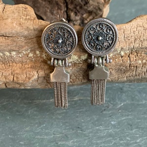 May include: A pair of silver earrings with a round, filigree design and a dangling chain tassel.