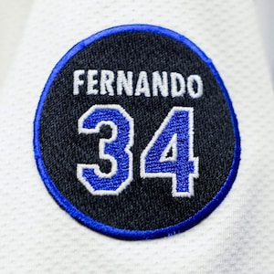 May include: A black and white embroidered patch with a blue border. The patch features the name "Fernando" and the number "34" in white with a blue outline.
