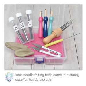 May include: A clear plastic case containing needle felting tools. The kit includes needles in labeled tubes, pink, blue, and wooden handled tools, scissors, and clay pieces. The case sits on a light wood surface.