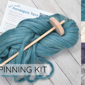 May include: A spinning kit with a large bundle of teal-colored handspun yarn and a wooden spindle. The kit includes instructions and a selection of other yarn colors. The words "SPINNING KIT" are displayed in white text.