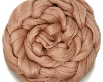 May include: A close-up of a large amount of light brown wool roving, twisted and piled into a circular shape.