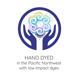 May include: A logo featuring a stylized, colorful floral design within a dark blue circle, held by two blue hands. The text "HAND DYED in the Pacific Northwest with low impact dyes" is below the design.