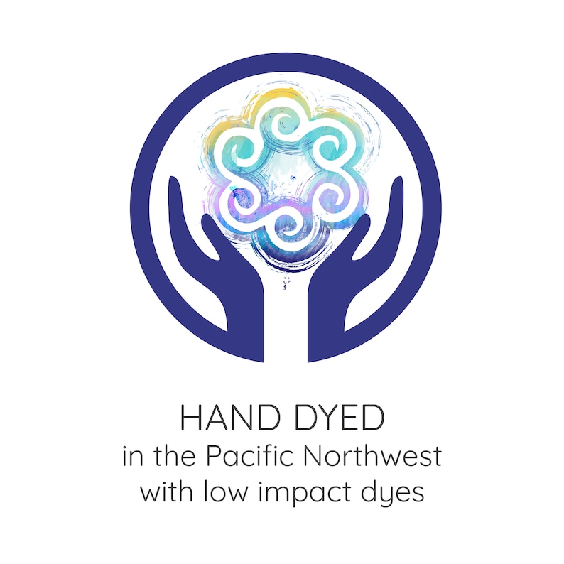 May include: A logo featuring a stylized, colorful floral design within a dark blue circle, held by two blue hands. The text "HAND DYED in the Pacific Northwest with low impact dyes" is below the design.