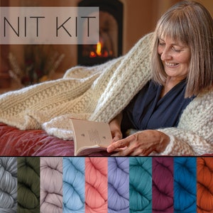 May include: A woman wrapped in a cream-colored, chunky knit blanket, reading a book. The image includes the text "KNIT KIT" at the top and a selection of colorful yarn skeins at the bottom. The blanket appears soft and warm.
