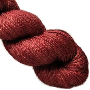 May include: A close-up of a skein of burgundy-colored yarn. The yarn appears soft and has a slight sheen, suggesting a luxurious fiber. The color is a deep, rich red with subtle variations in tone.