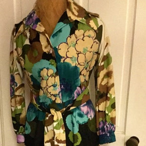 May include: A long-sleeved dress with a floral print in shades of brown, green, blue, and purple. The dress has a button-up front and a belt.