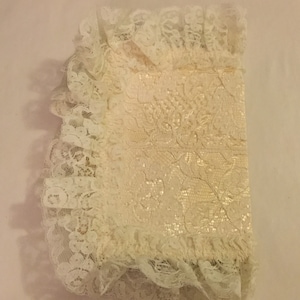 K&ouml;nnte beinhalten: Ein wei&szlig;er Spitzenstoff mit einem Blumenmuster. Die Spitze ist gefaltet und hat einen gekr&auml;uselten Rand.