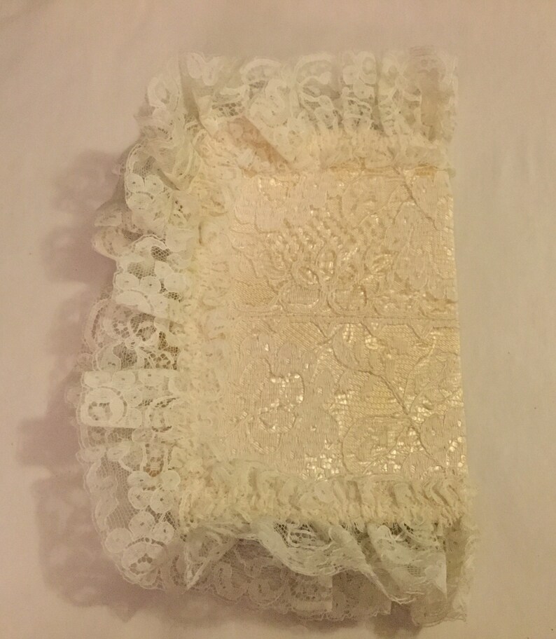 K&ouml;nnte beinhalten: Ein wei&szlig;er Spitzenstoff mit einem Blumenmuster. Die Spitze ist gefaltet und hat einen gekr&auml;uselten Rand.