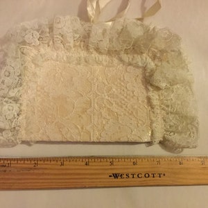 K&ouml;nnte beinhalten: Eine wei&szlig;e Stofftasche mit einem zarten Blumenmuster, die mit Spitze verziert ist. Die Tasche ist etwa 20 cm breit.