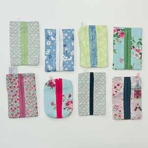 May include: A collection of eight fabric pouches in various patterns and colors. Designs include floral, cloud, and geometric patterns. Each pouch has a contrasting vertical stripe and a small loop at the top.