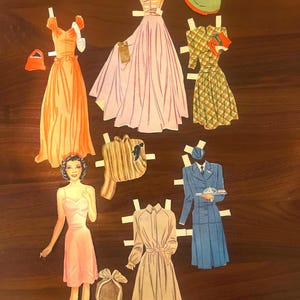 May include: Vintage paper doll set featuring a female figure and various outfits. The outfits include dresses, a suit, and accessories in shades of orange, pink, green, and blue. The doll and clothing are cut out with tabs for attachment.