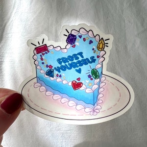 May include: A blue heart-shaped cake with pink frosting and colorful sprinkles. The cake has the text "Frost Yourself" written on it.