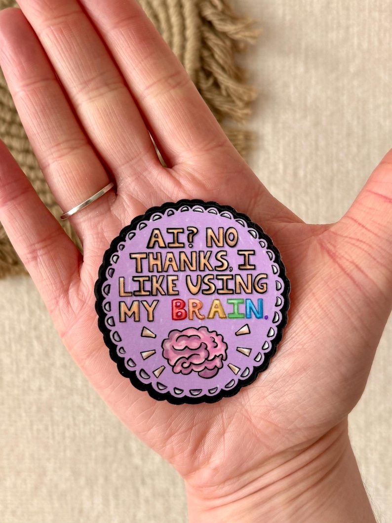 May include: A round sticker with a scalloped black border and the text "AI? NO THANKS, I LIKE USING MY BRAIN." The sticker has a light purple background with a pink brain graphic and colorful text.