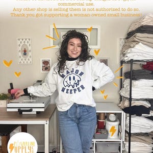 May include: A woman wearing a white sweatshirt with the text "MAJOR WEEPER" in navy blue, paired with blue jeans. The image includes a heat press machine, storage shelves, and the "POWERLINE SUPPLY CO." logo.