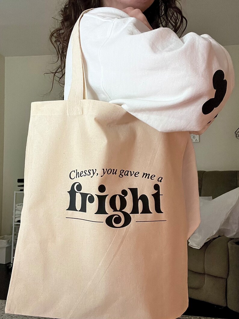 Op de afbeelding: Een beige tote bag met zwarte tekst die "Chessy, you gave me a fright" luidt. De tekst is in een vetgedrukt, decoratief lettertype.