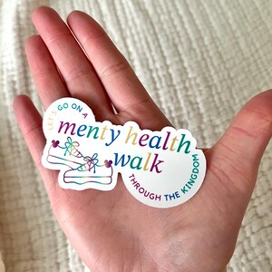 以下が含まれることがあります： 「Let's go on a mental health walk through the kingdom」というテキストと、靴ひもにハートが付いたスニーカーのペアが描かれたカラフルなステッカーです。