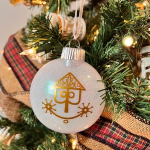 May include: A white glitter Christmas ornament with a gold house design and a gold star on each side. The ornament is hanging on a Christmas tree.