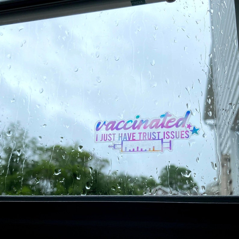 K&ouml;nnte beinhalten: Ein Aufkleber an einem Fenster mit Regentropfen. Der Aufkleber ist ein Regenbogen-Verlauf und sagt "geimpft ich habe nur Vertrauensprobleme" mit einer Spritzengrafik.