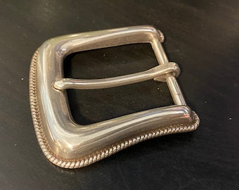 Könnte beinhalten: Silberne Gürtelschnalle mit einem Seil-Design am Rand.